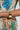 A person in a textured, colorful floral outfit is shown from the waist up, wearing the KEY TO MY HEART CUFF bracelet featuring a small ornate design. The background is light and plain.