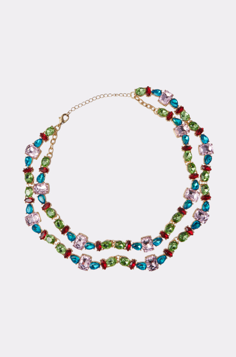 The I WANT IT ALL NECKLACE is a double-layered statement piece with rectangular and oval multicolored gemstones in a gold-tone setting, featuring an adjustable chain clasp for a striking, repeating look.