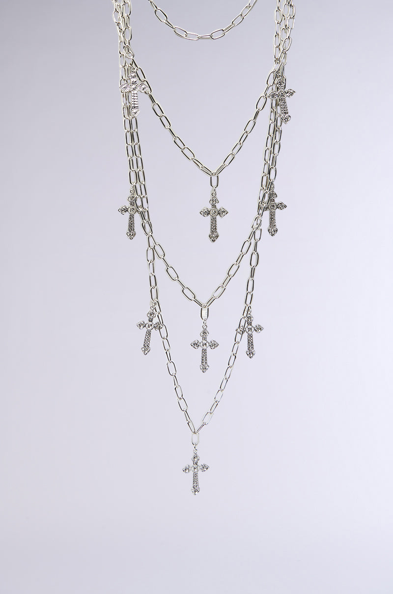 The LAYERS TO THIS CROSS NECKLACE features multiple thin faux silver chains, each with rhinestone-studded cross pendants, displayed against a plain light gray background. 2