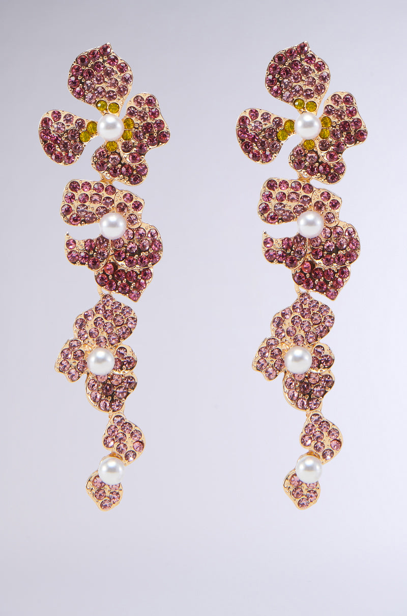 A pair of FLOWER POWER EARRINGS from YIWU MASTER with a floral design, featuring pink gemstones and small pearls embedded in a gold setting. Each earring showcases a cascading arrangement of flower shapes with intricate detailing, set against a plain gradient background transitioning from light to dark gray.