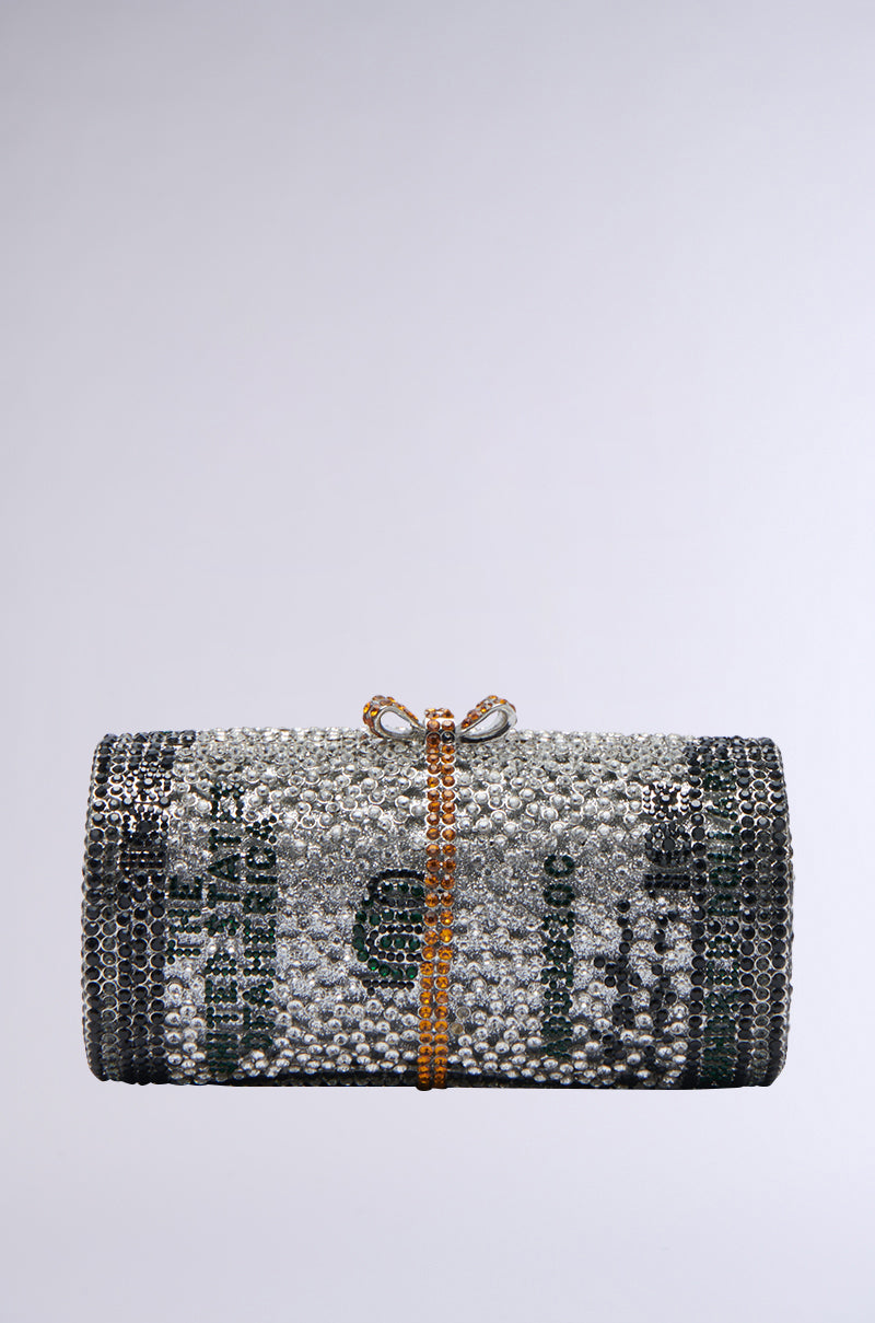 The MONEY ON MY MIND BLING CLUTCH is a dazzling novelty handbag adorned with rhinestones, styled to resemble a rolled-up dollar bill. This horizontally oriented purse features a gold bow accent on top, set against a simple light gray backdrop.
