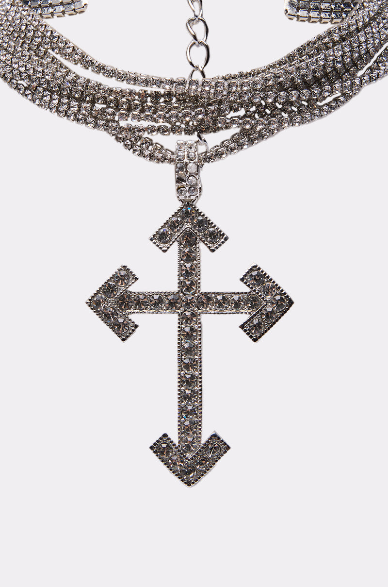 A close-up of the CROSS MY HEART CHOKER, a silver necklace featuring a large rhinestone-studded cross charm with arrow-shaped ends, displayed on a white background. 3