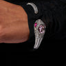 A close-up of a person's wrist adorned with the NIKKI SNAKE BRACELET. This flexible, snake-shaped bracelet, encrusted with sparkling rhinestone embellishments and featuring prominent pink gemstones for the eyes and head, contrasts strikingly against the black fabric draping the arm.