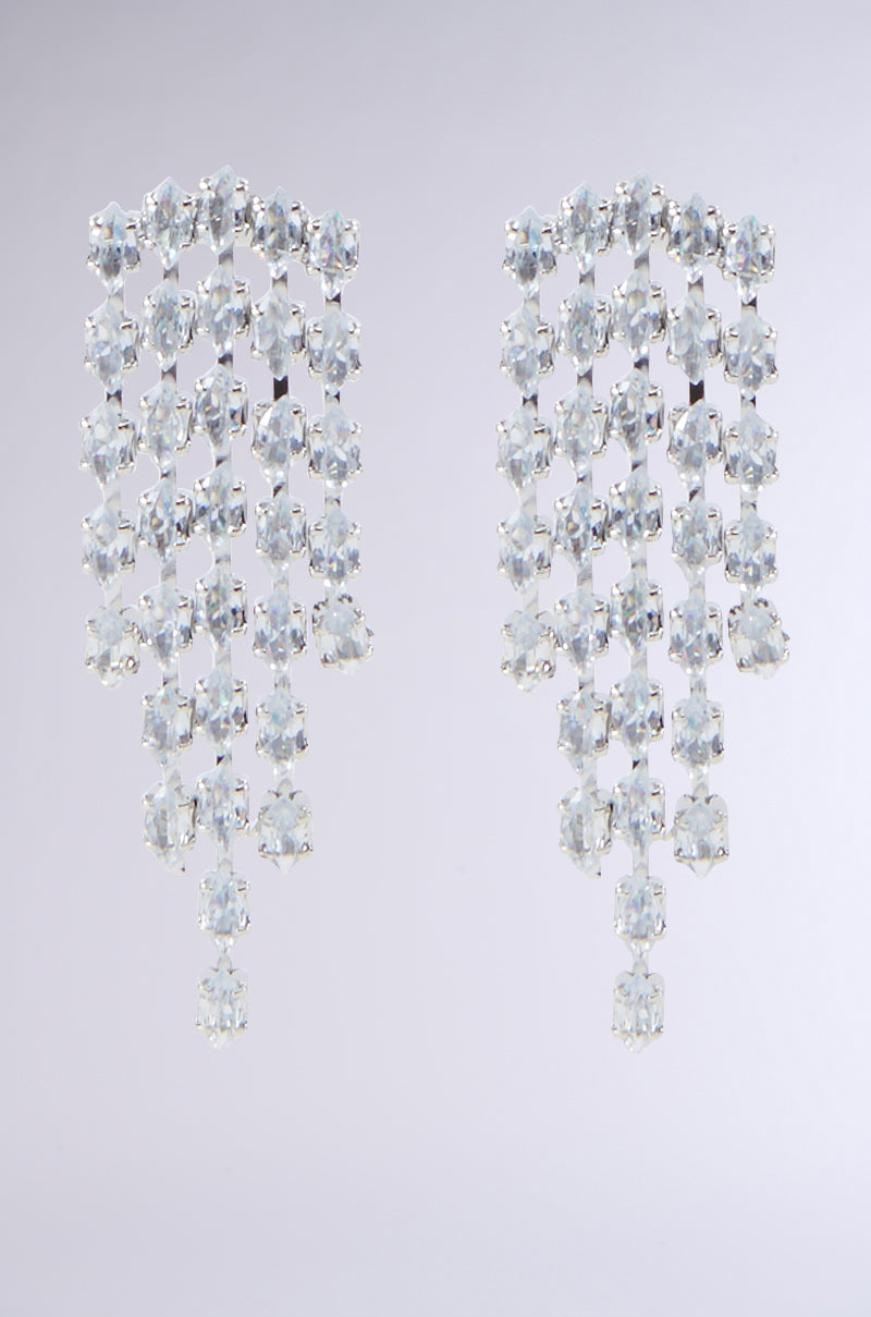 The IM EXPENSIVE EARRING from the AKIRA Label showcases multiple rows of sparkling, clear crystal gemstones complemented by rhinestone accents that cascade in a beautiful waterfall style. These elegant dangle earrings exude luxury and dazzle against a plain gray background.