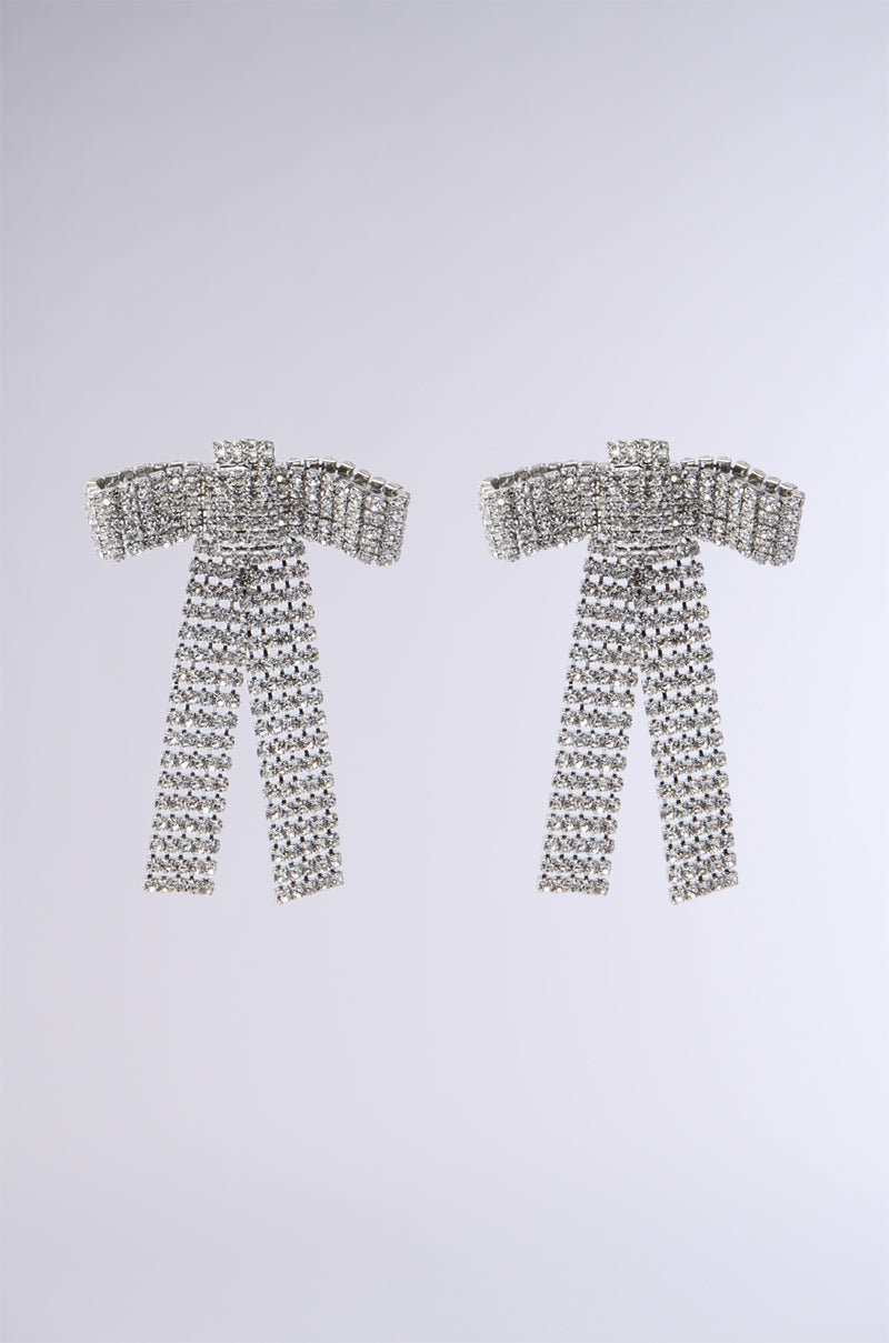 The BOO UP EARRING exudes elegance with its sparkling bow-shaped silhouette, adorned with rows of scintillating rhinestones. It features a knotted top and cascading strands that create a luxurious and dazzling effect against a plain, light gray background.