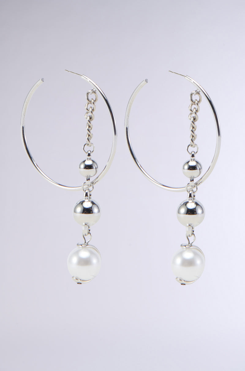 Introducing the DROP OUT EARRING – a pair of metallic silver hoop earrings featuring elegant dangling elements. Each earring showcases a chain link adorned with a small silver bead, a larger silver bead, and a faux pearl bead at the bottom, resulting in a beautifully layered design. The background remains plain and light to highlight their sophistication.