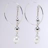 Introducing the DROP OUT EARRING – a pair of metallic silver hoop earrings featuring elegant dangling elements. Each earring showcases a chain link adorned with a small silver bead, a larger silver bead, and a faux pearl bead at the bottom, resulting in a beautifully layered design. The background remains plain and light to highlight their sophistication.