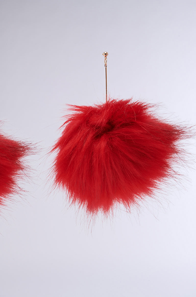 MAMI FUR EARRING is a fuzzy red faux fur ball accessory featuring a fine golden string at the top, adorned with oversized dangle fur detail, set against a plain light gray background. 3