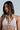 A woman with long, dark hair wears a white top with pearl strands in a crisscross design. A Pearl Goddess Hair Clip Set elegantly tames her tresses as she gazes sideways against a light background.
