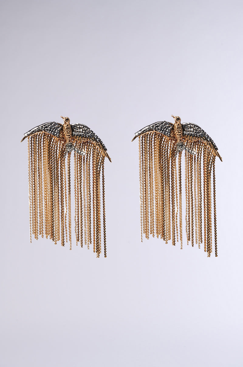 The FLY AWAY EARRING features gold-tone bird-shaped designs with textured wings and detailed bodies, complemented by cascading chainlink fringes that enhance its elegance against a plain background.