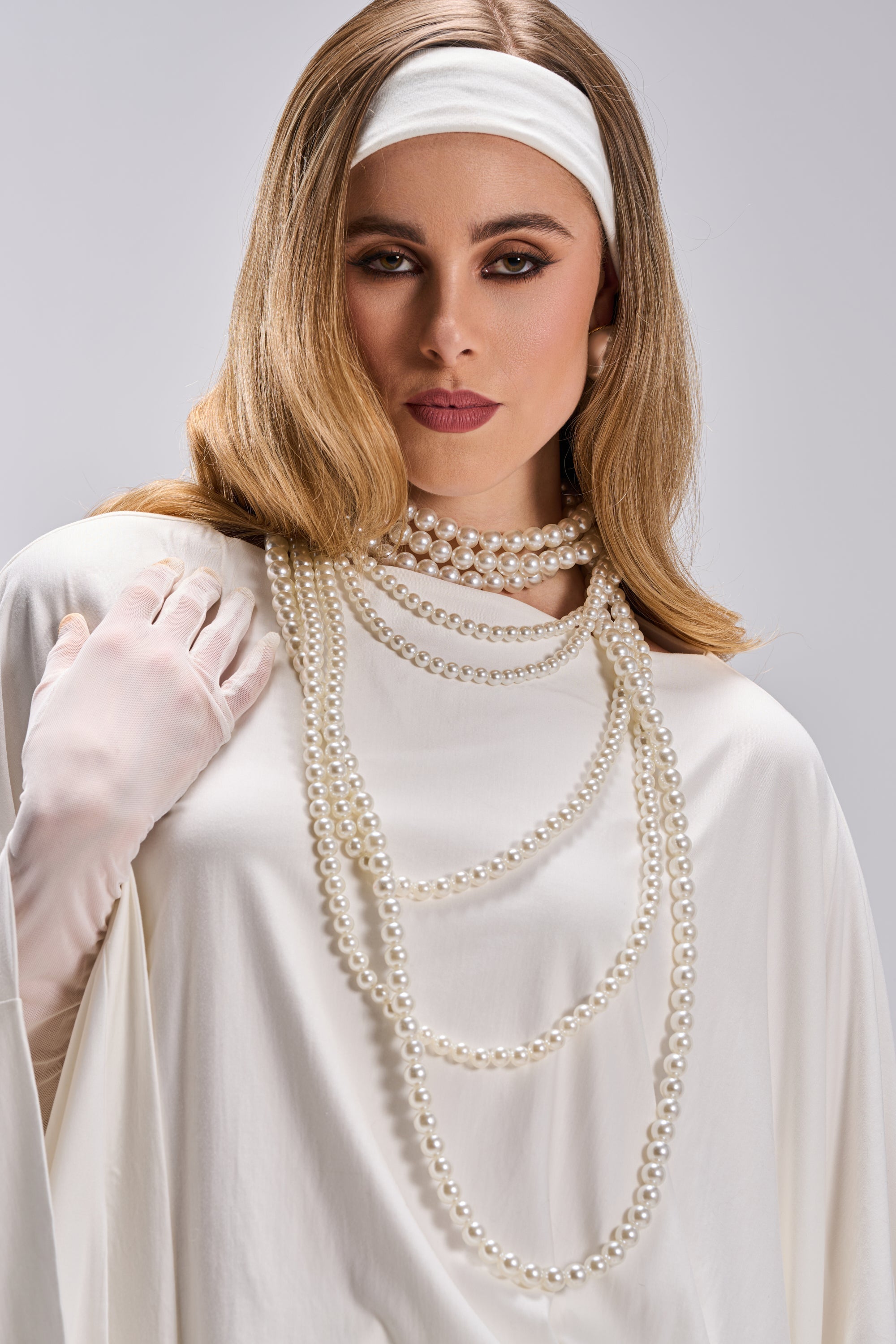 A woman in a white dress with long gloves and the PENELOPE STATEMENT PEARL NECKLACE poses against a plain gray background; she has straight light brown hair, a white headband, and wears neutral makeup. 1