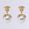 The MANSION VIBES EARRING features elegant gold-tone drop earrings adorned with intricate lion head designs at the top and large faux pearl-like orbs hanging below, accented by small crystal details—perfect for those who love a touch of sophistication.