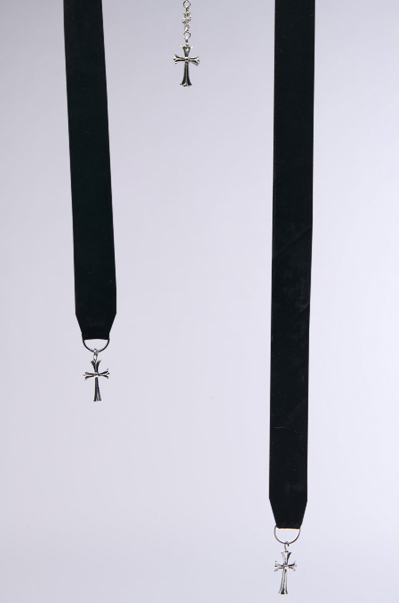 Two CROSS MY HEART STATEMENT NECKLACES with black ribbon chokers feature silver cross pendants adorned with striking black gemstones, hanging vertically against a plain background. Above them, a smaller cross charm elegantly dangles from a chain, completing this statement necklace ensemble.