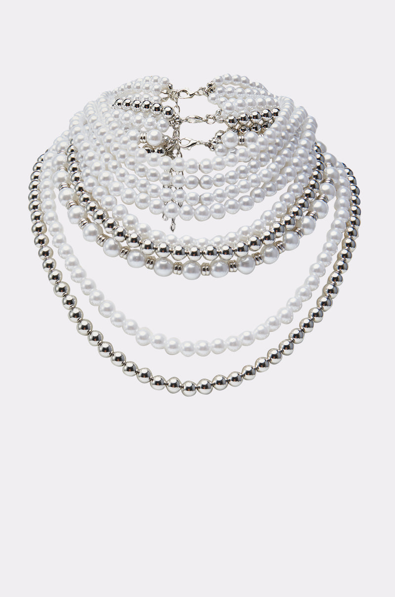 The REGAL VIBES LAYERED NECKLACE features alternating strands of white pearls and shiny silver beads, arranged in a semicircle on a plain light background for an elegant, regal look.