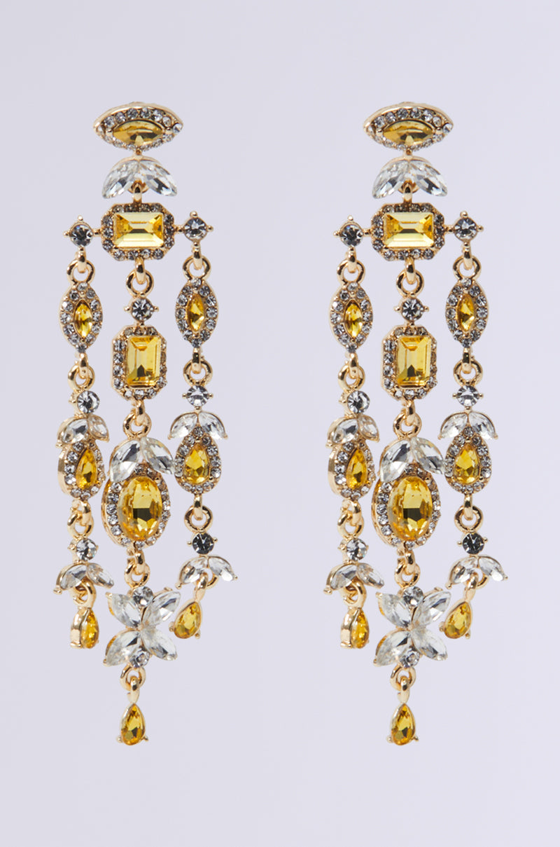 The KATE STATEMENT EARRING showcases a stunning design with intricate gold chandelier earrings embellished with yellow and clear gemstones in teardrop and oval shapes. They feature a rhinestone-encrusted trim and delicate floral accents, adding an elegant touch to any ensemble.