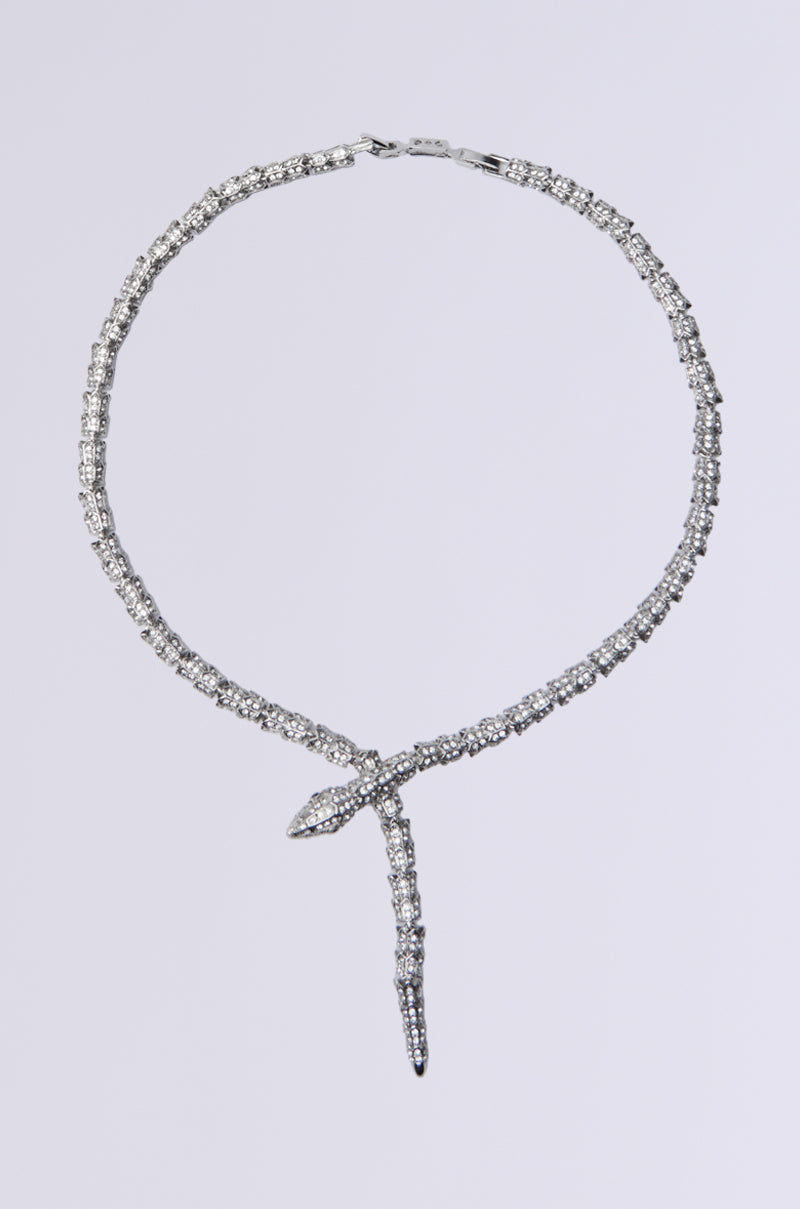 The "I PREFER WEALTH CZ STONE NECKLACE" is a captivating piece, featuring a snake silhouette adorned with sparkling rhinestones, elegantly designed with a loop and pointed tail, set against a plain gray background.