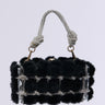 The IT GIRL FAUX FUR CLUTCH is a luxurious black faux fur clutch with silver embellishments, a rhinestone-studded chain handle, and an intricately knotted design. Its metallic snap-top closure adds sophistication against a plain white background.