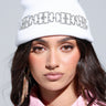 A person wearing a KIKI Rhinestone Beanie adorned with a chain design and paired with long, sparkling earrings. Their dark hair complements the pink collared shirt they are dressed in, while the neutral background highlights their striking accessories.