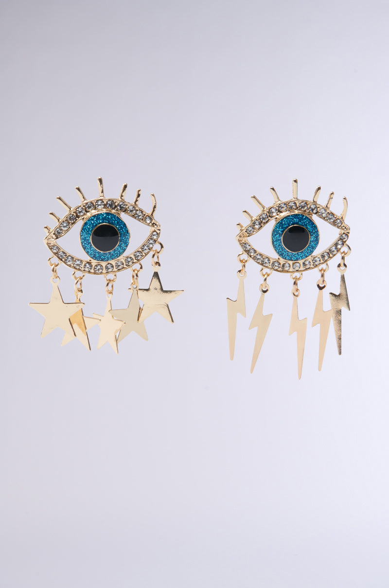 The "ALL EYES ON ME GOLD EARRING" features eye-shaped gold earrings with blue centers, enhanced by rhinestones, and adorned with dangling gold star and lightning bolt charms on a light gray background.