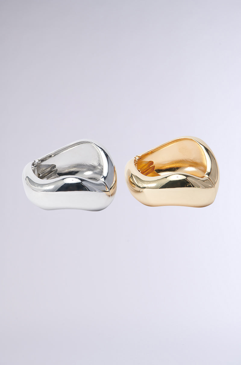 Two chunky rings, resembling the YOUR ICON BRACELET CUFF SET, are showcased against a light background. One ring is crafted in silver and the other shines in gold. Both feature smooth, curved designs with reflective surfaces that evoke the timeless style of an iconic bracelet collection.