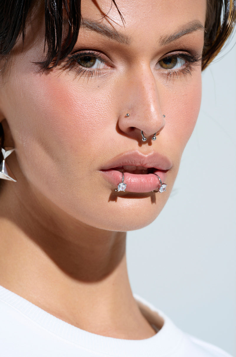 A close-up shows a person with multiple facial piercings, featuring the SO ORIGINAL LIP CUFF SET, including a faux silver nose ring, stud, and septum ring. They wear rhinestone-studded star earrings and have a neutral expression with minimal makeup.
