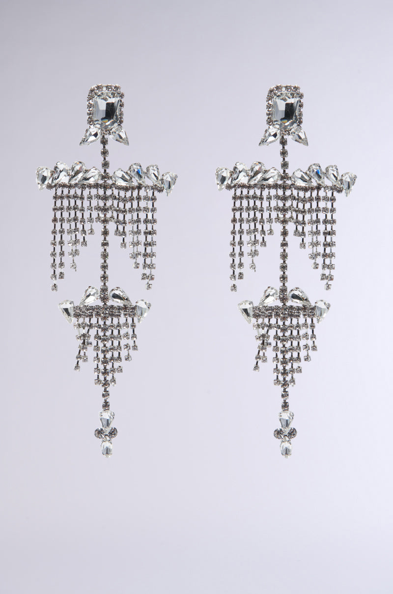 Introducing the ALL NIGHT LONG STATEMENT EARRING: a stunning pair of chandelier earrings adorned with elaborate crystal patterns, teardrop-shaped jewels, and multiple layers of shimmering rhinestones set against a simple backdrop.
