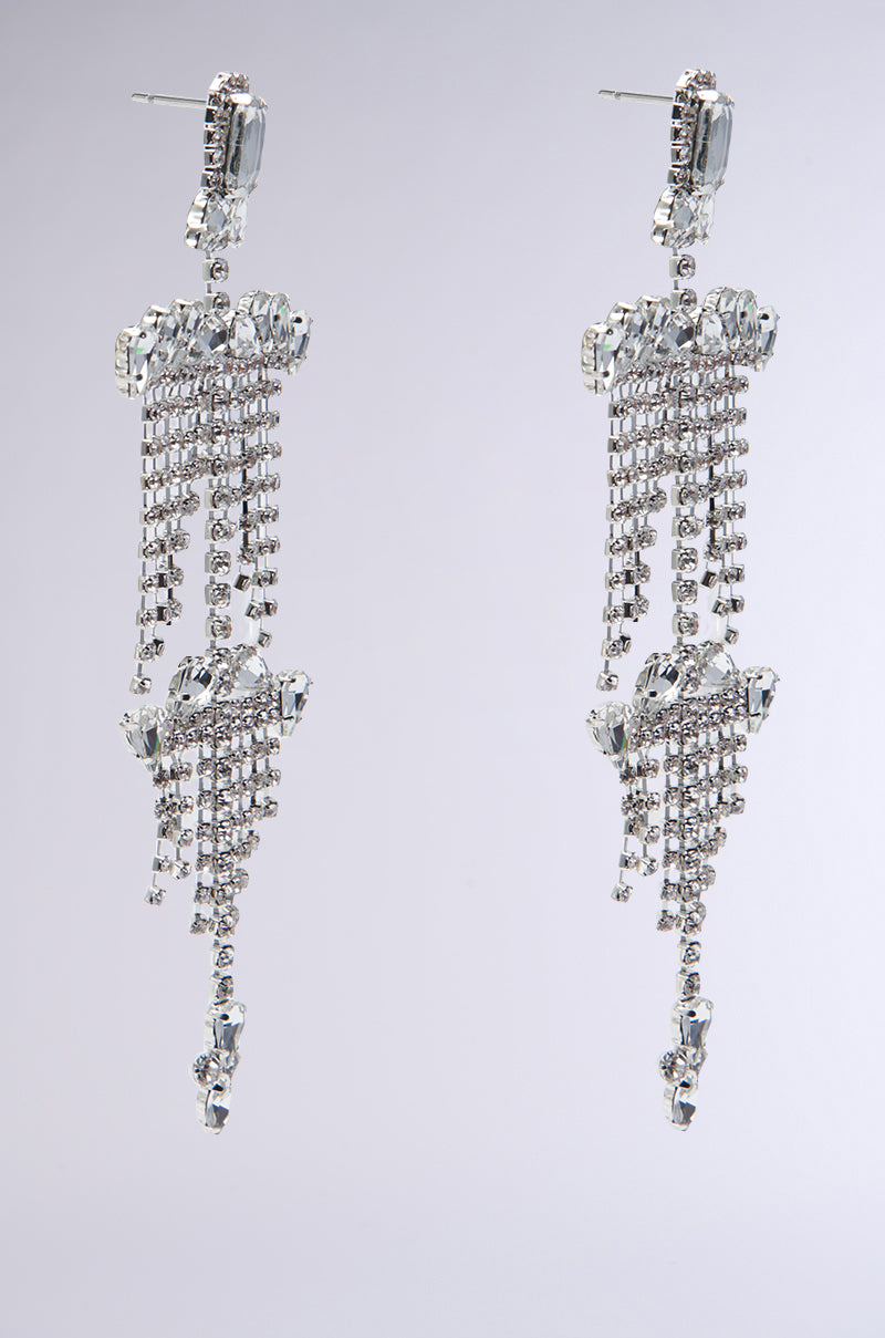 Introducing the ALL NIGHT LONG STATEMENT EARRING, featuring long silver chandelier design with intricate beadwork. These earrings are adorned with dangling strands and sparkling rhinestone links, set against a plain background. The teardrop-shaped jewels beautifully catch the light, making these earrings a true statement piece.