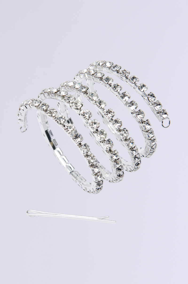 The NEVER SPIRALING BLING PONY WRAP is a coiled, silver bejeweled headband with rhinestone embellishments, paired with a single silver bobby pin, displayed on a plain white background. This elegant accessory adds the perfect sparkle to any style.