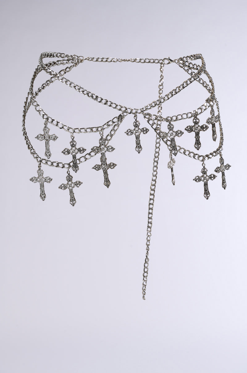 The CROSS MY HEART CHAIN BELT is a faux silver chain link belt with ornate cross charms, offering a gothic style. Its layered chains provide texture and complexity against a plain white background.