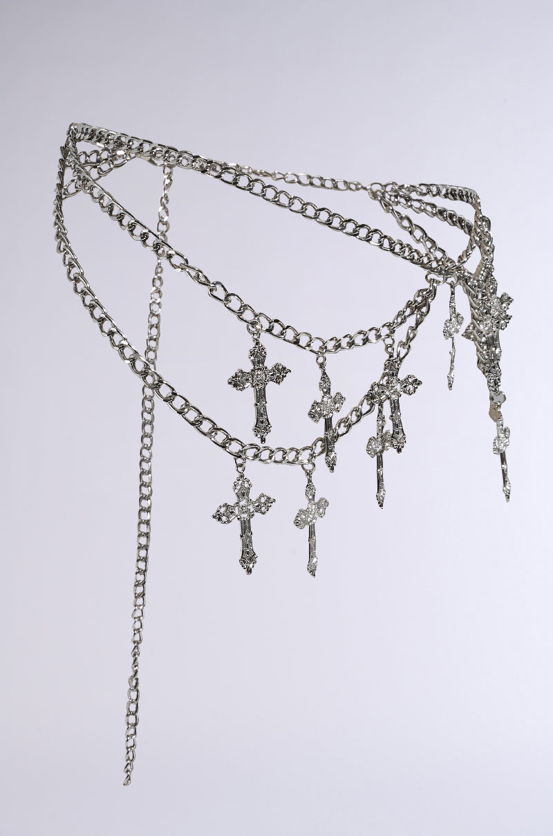 The CROSS MY HEART CHAIN BELT is a faux silver accessory with multiple layers and cross-shaped charms, elegantly displayed against a plain gray background. Its intricate chain link design enhances its sophisticated appeal.