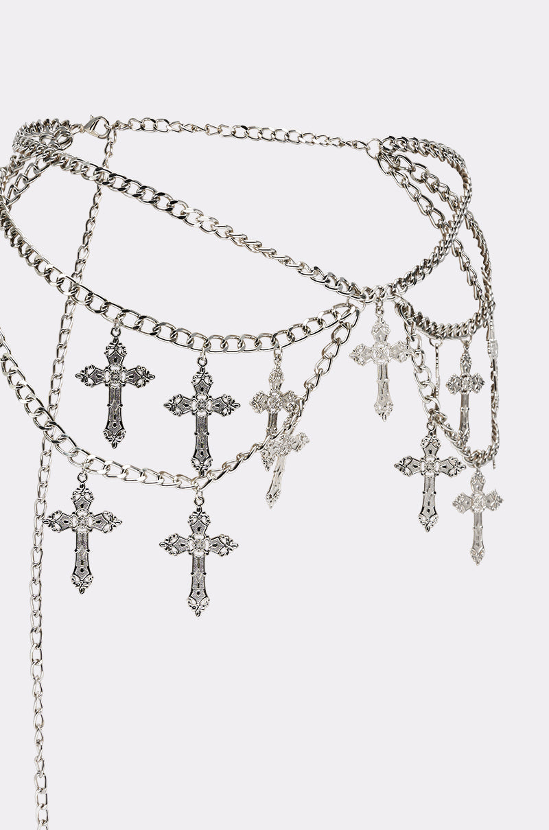 The CROSS MY HEART CHAIN BELT is a silver chain belt adorned with multiple dangling cross charms in different sizes, shown on a plain white background. 3