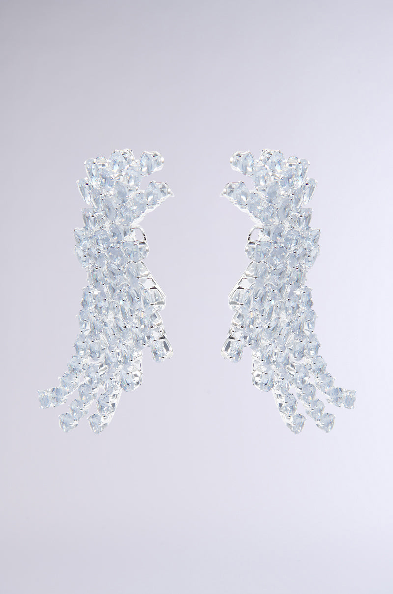 Close-up of TAYTAY STATEMENT EARRINGS, designed as profiles of faces embellished with teardrop rhinestones. These intricate earrings create a shimmering and elegant effect against a light gray background. 3