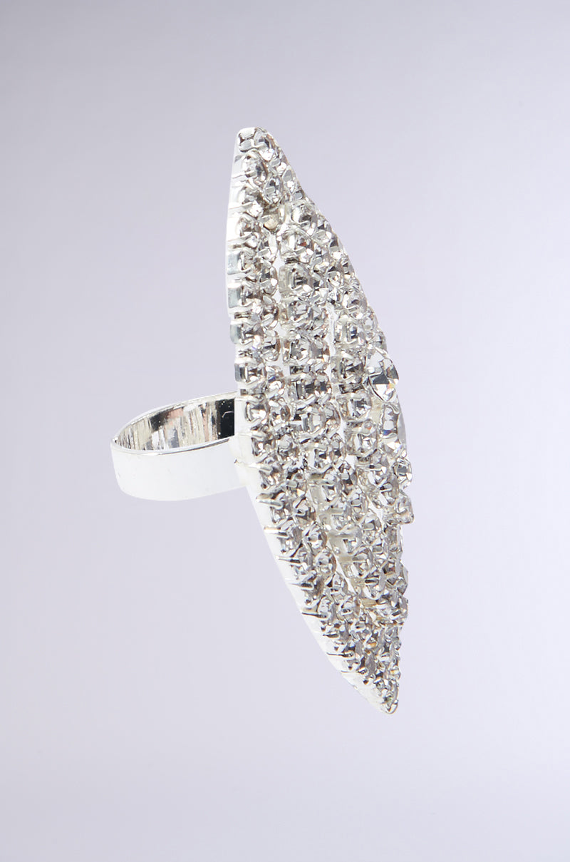 The SEE DIAMONDS COCKTAIL RING, featuring a wide band and an elongated oval shape adorned with numerous small, sparkling rhinestones, is displayed against a plain, light background.