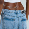 A person in light blue jeans and a white crop top elegantly sports the ENTICING BODY CHAIN over their waistband, while a hint of black and white striped fabric peeks out from the back pocket for added flair.