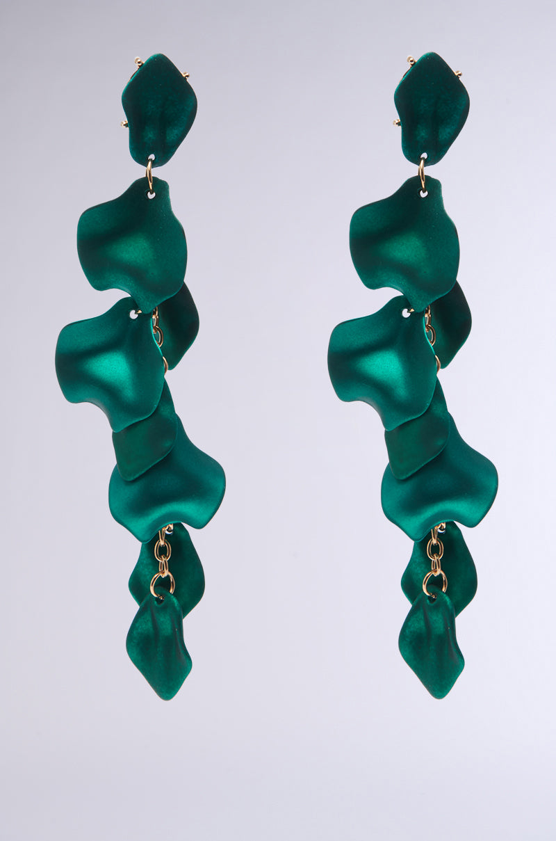 Emerald green NO ENVY PETAL EARRINGS, featuring a wavy petal design and layered structure connected by small faux gold links, hang elegantly against a light grey background.