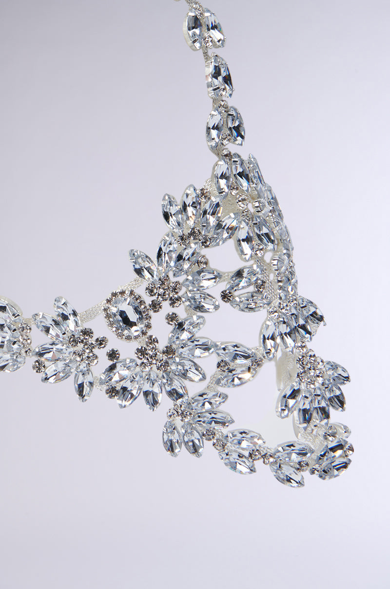 Close-up of the TAKE MY PIC STATEMENT HEADPIECE, an ornate, silver piece encrusted with jewels, featuring intricate floral and leaf patterns adorned with sparkling crystals and teardrop gemstone embellishments against a plain background. 4