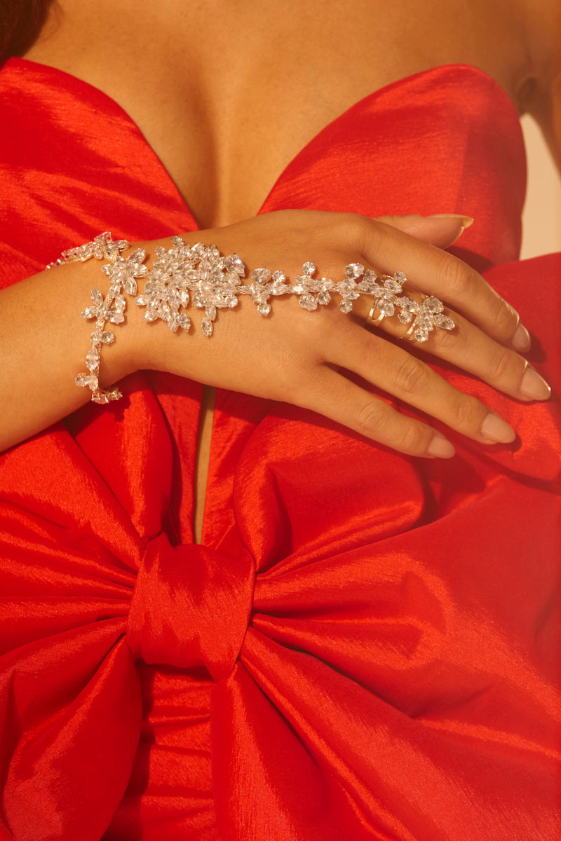 A woman wearing a red satin dress with a large bow, adorned with the I SHOW UP BRACELET RING that drapes elegantly and sparkles on her hand and wrist.