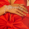 A woman wearing a red satin dress with a large bow, adorned with the I SHOW UP BRACELET RING that drapes elegantly and sparkles on her hand and wrist.