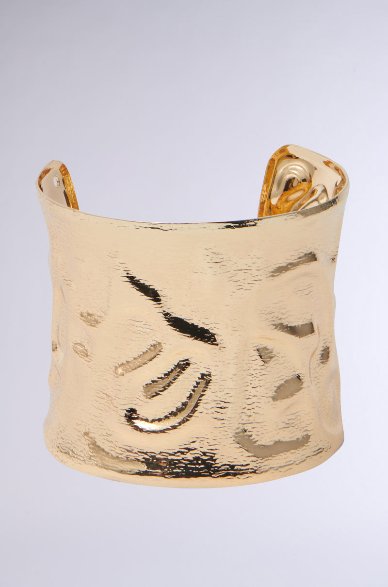 The GOLDEN GODDESS CUFF is a bold, wide gold cuff bracelet with an open back and a textured, hammered design, perfect for making a statement against any background.