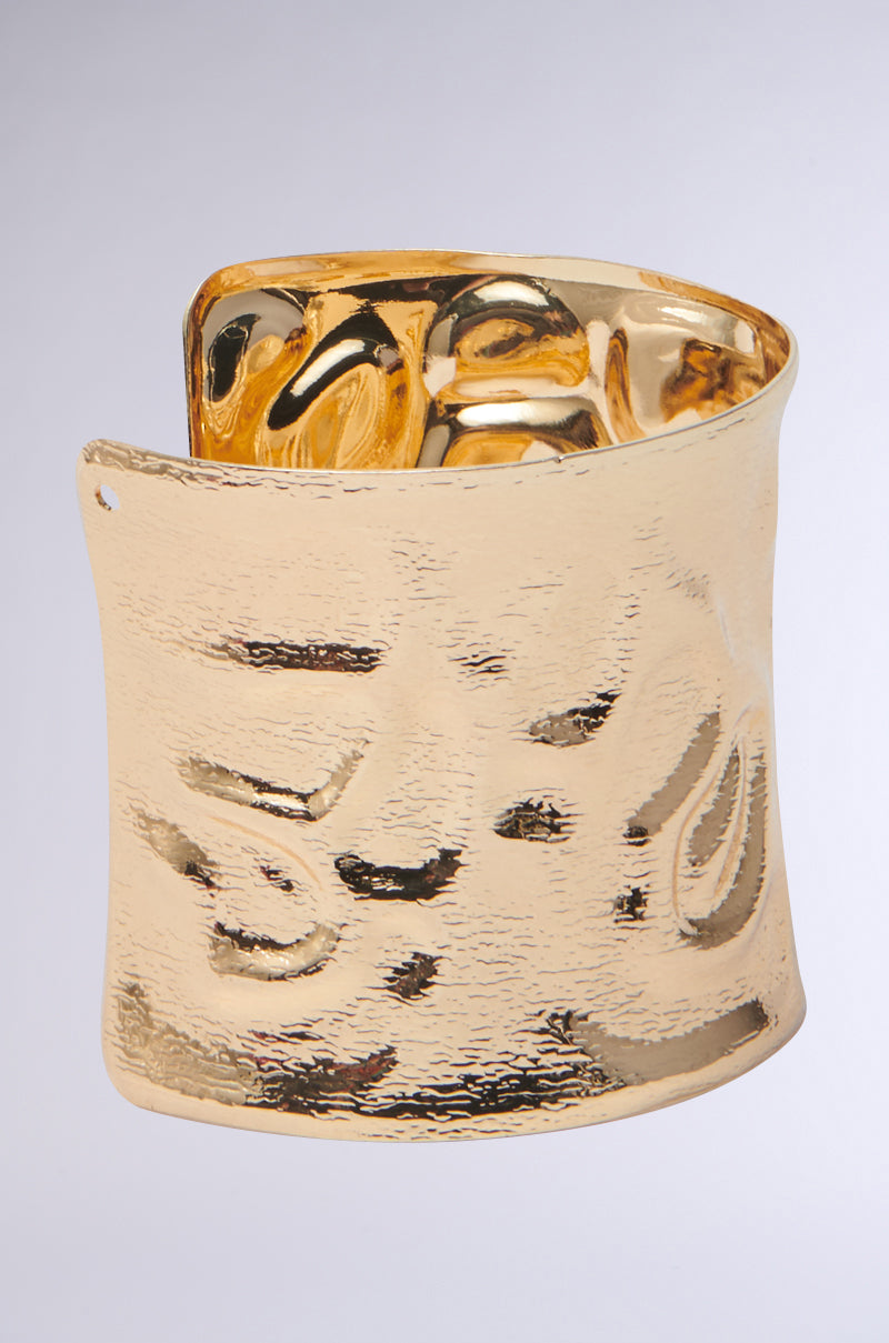 The GOLDEN GODDESS CUFF features a wide, hammered design with a textured, shiny finish—this bold bracelet stands out beautifully against a plain light gray background.