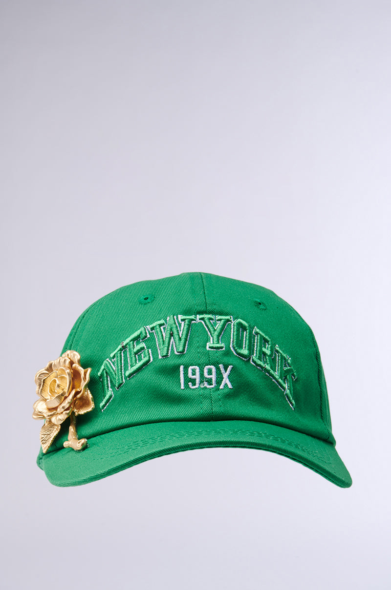 The THIS IS MY CITY HAT is a green baseball cap embroidered with "NEW YORK" and "199X" in white, featuring a gold rose on the front left. It has an adjustable strap and is set against a plain light gray background. 2
