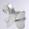An abstract silver sculpture features interlocking curves and angles against a light gray background. Reminiscent of a modern accessory like the KANDYCE BRACELET, it has an artistic design with a smooth metallic finish.