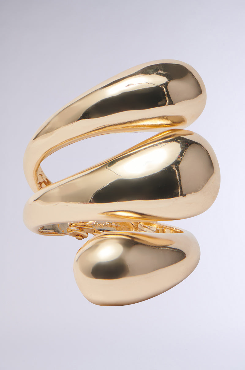 A polished, abstract sculpture that mimics a luxury cuff bracelet, resembling the IT IS WHAT IT IS BRACELET CUFF with smooth curves and a faux gold finish, set against a plain background. 0