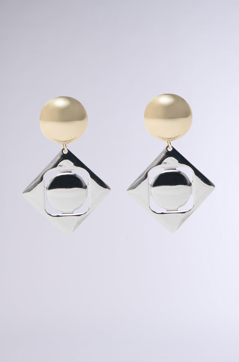 Introducing the SQUARE UP EARRING IN SILVER, featuring circular gold tops and square silver pendants with circular centers. This minimalist geometric design is crafted on a sleek metallic base against a light gray gradient background, creating a stunning visual appeal.