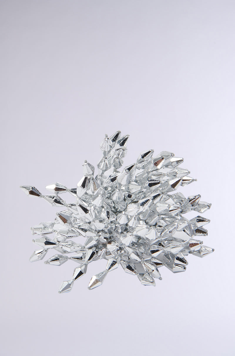 The TAKE MY POWER RING features a starburst pattern of reflective faux silver geometric shapes against a white background. The sharp, shiny angles resemble metallic crystals, creating an eye-catching appearance reminiscent of this statement ring.