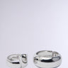 The ESSENTIAL BANGLE SET features two shiny faux silver bracelets on a plain gray background: a smaller flat bangle on the left and a larger rounder one on the right. Both have a sleek, reflective finish.