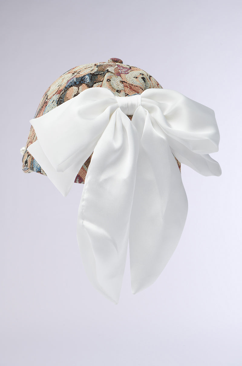The BEARY NICE BOW HAT is a baseball cap with a gray cotton tapestry design in muted colors and a large, elegant white satin bow at the back.