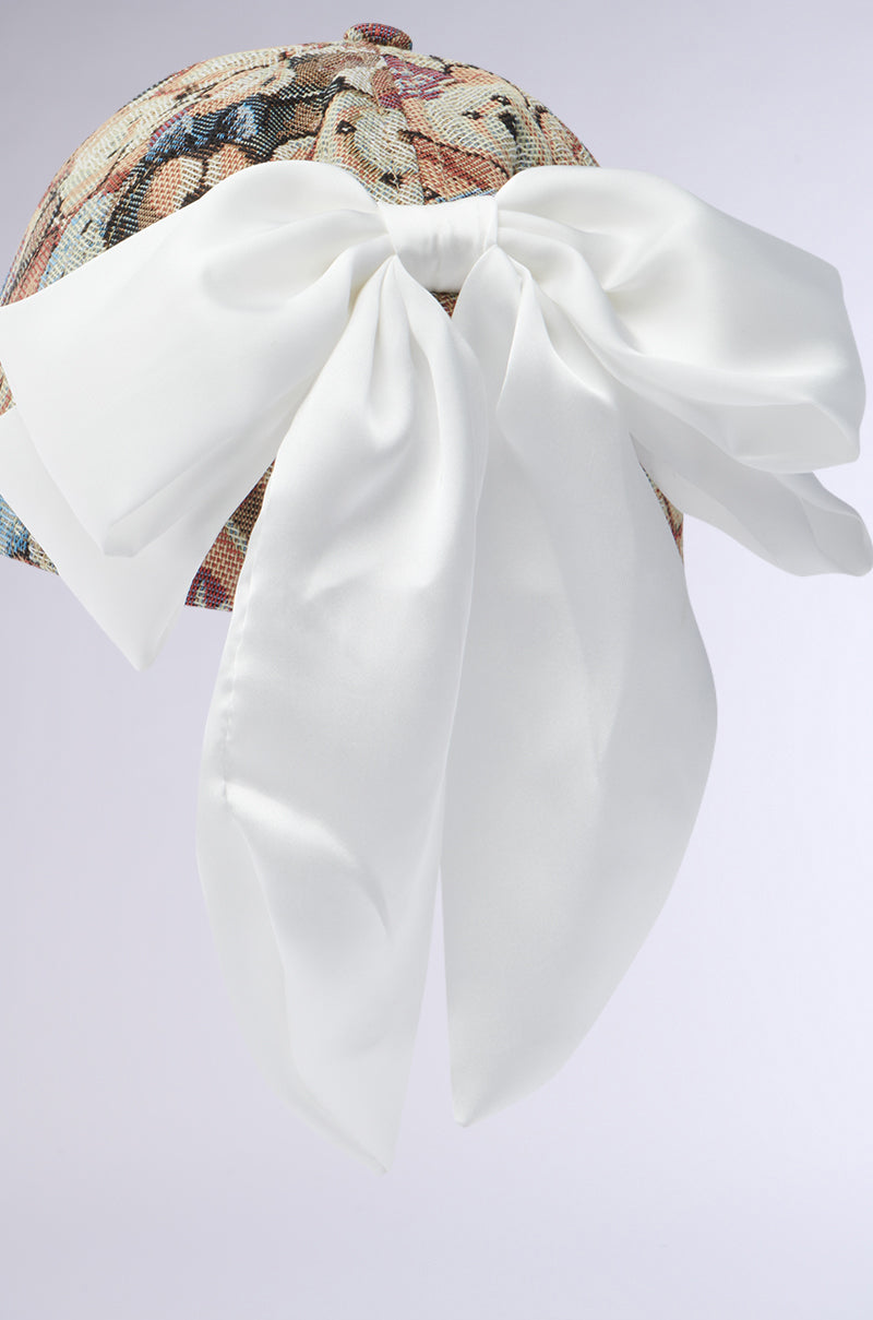 A close-up of the BEARY NICE BOW HAT shows a floral-patterned baseball cap with an elegant silk bow tied at the back, perfectly complemented by a neutral light gray backdrop.
