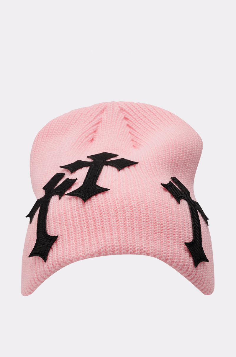 The CROSS ME BEANIE is a light pink knit beanie with three large black gothic cross appliqués on the front and sides, shown against a white background—ideal for making bold style statements. 1