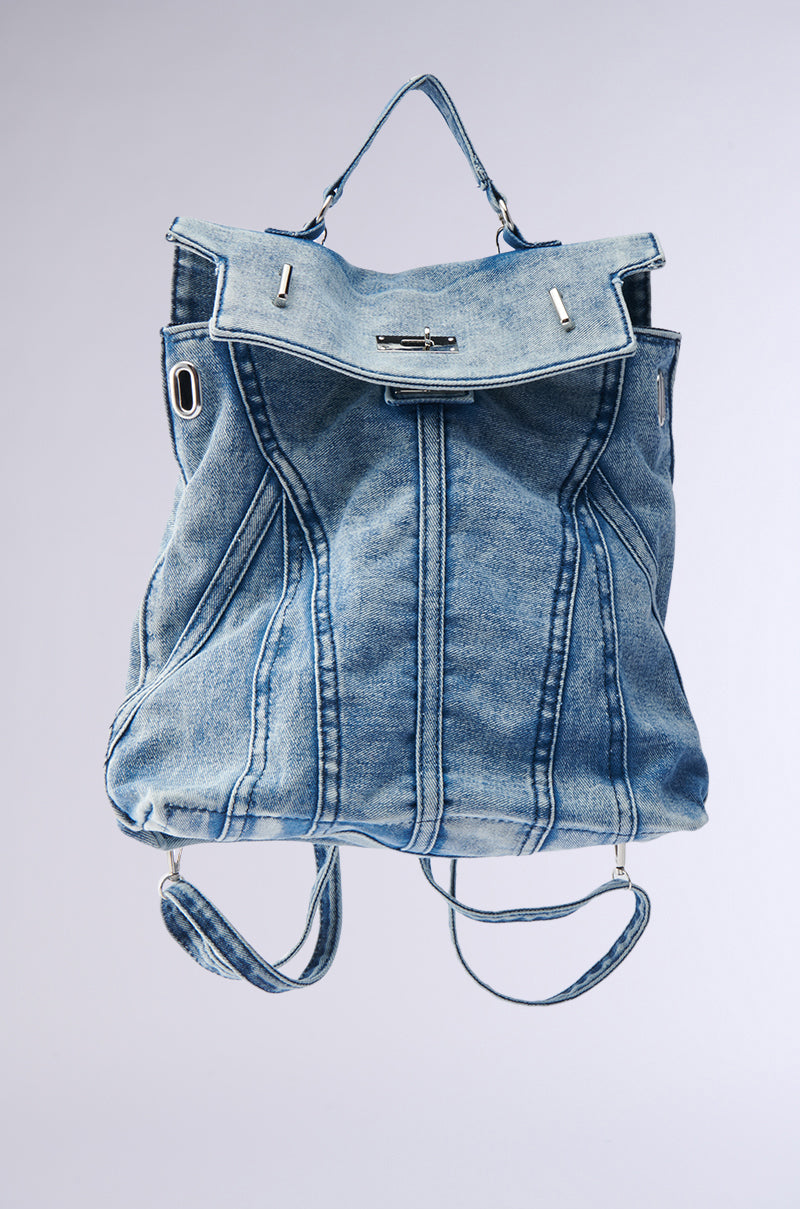 The KEEP EM ALL BACKPACK is a blue denim bag with visible seams, silver hardware, a top handle, and adjustable shoulder straps. This versatile accessory is shown against a light gray background. 1